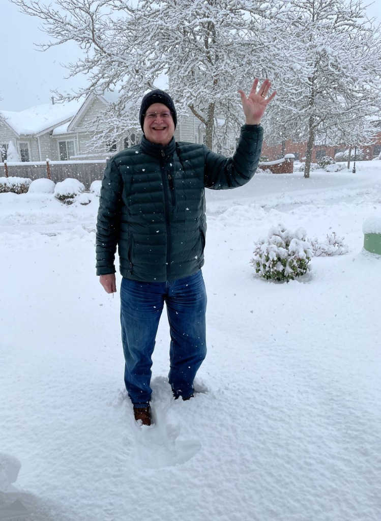 man standing in snow, waving, while snow continues to fall